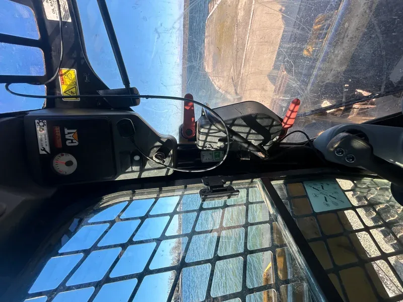 View from inside a skid steer cab with controls and mirror