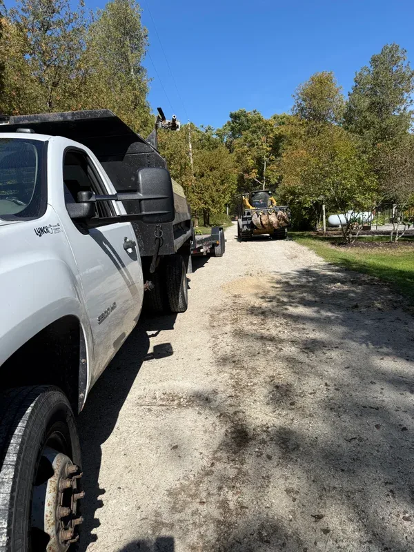 GMC dump truck beside a skid steer loading debris on a gravel drive