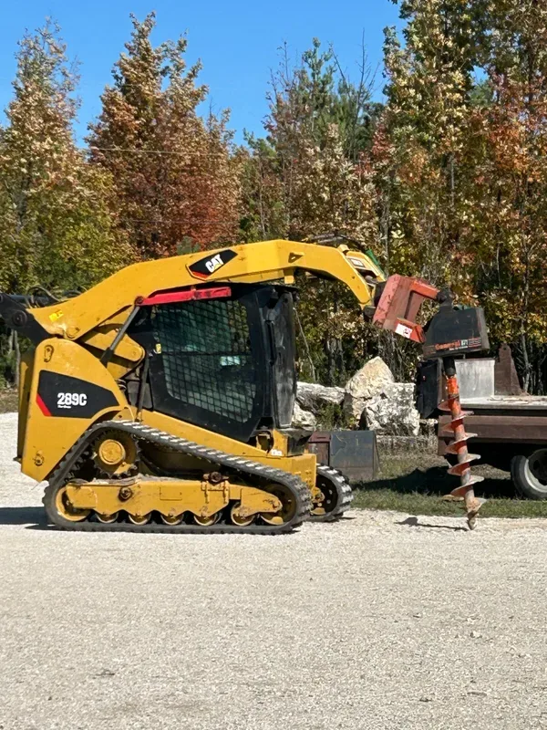 Skid steer with an auger attachment beside landscaping stone