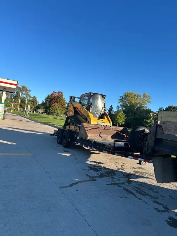 Skid steer on a flatbed trailer beside a truck on a paved drive