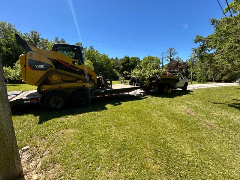Skid steer loaded on a trailer behind a dump truck