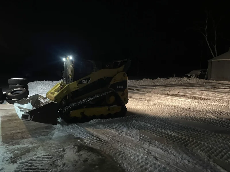 Skid steer clearing snow from a lot at night
