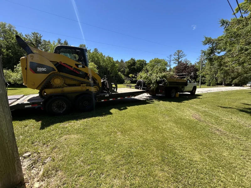 Skid steer loaded on a trailer behind a truck hauling cut brush